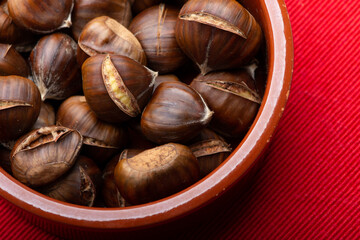 top down close up of roast chestnuts in a brown bowl with red background
