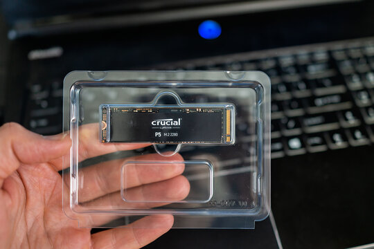 Banner Elk, USA - June 23, 2021: Macro closeup of hand holding Crucial micro chip by Micron and laptop computer keyboard for replacing dead hard drive