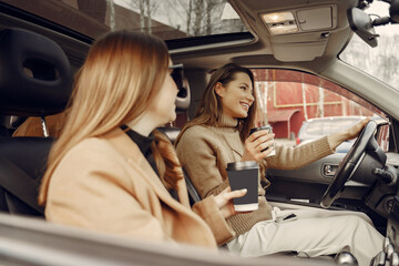 Three girls sitting inside the car and drinking a coffee