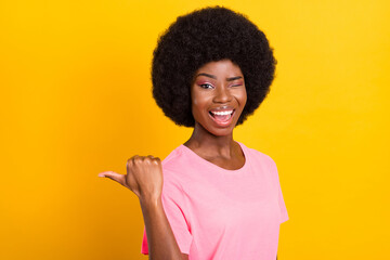 Profile side photo of young black girl happy smile wink eye point thumb empty space advertise isolated over yellow color background