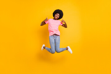 Fototapeta na wymiar Full size photo of cool millennial lady jump show thumb up wear pink t-shirt jeans isolated on yellow color background