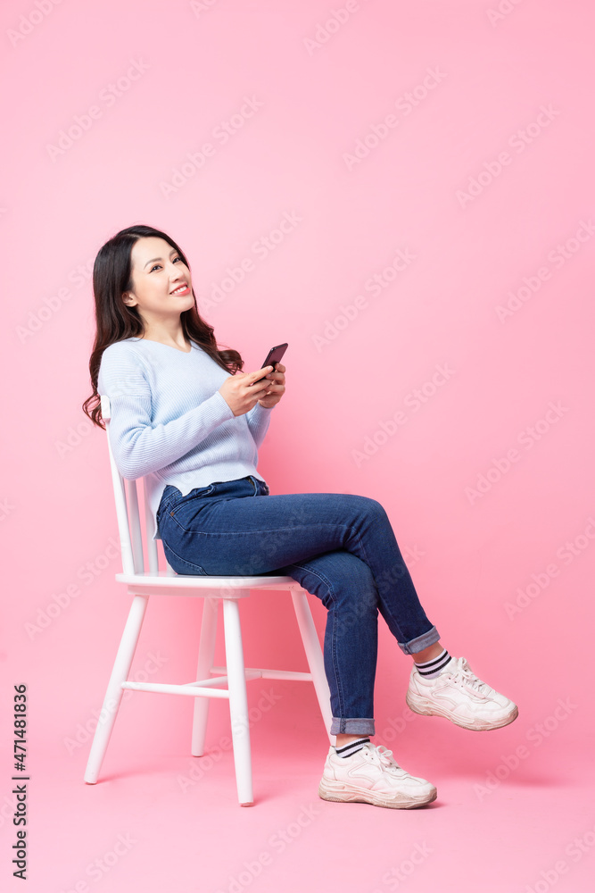 Wall mural portrait of beautiful asian girl sitting in chair, isolated on pink background