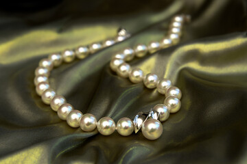 A pearl necklace of beads lies on a light green satin fabric with a golden sheen. Selective focus.