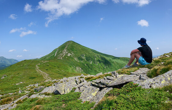 A man in a black hat sits on the slope of the Montenegrin ridge in the Carpathians and looks at Hoverla, the highest mountain in Ukraine
