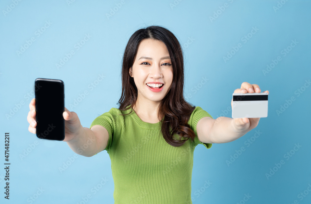 Wall mural portrait of young asian girl, holding phone, isolated on blue background