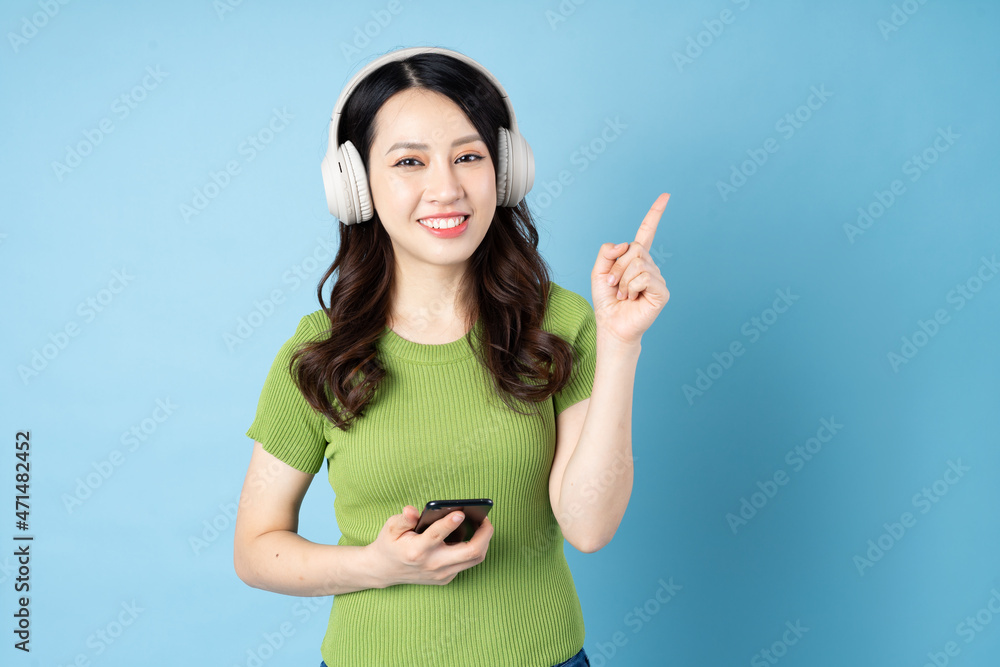 Wall mural Asian grasshopper girl portrait is listening to music, isolated on blue background