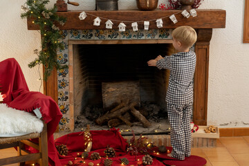 Niño con pijama calentandose las manos en la chimenea decorada de navidad 