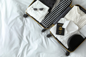 Open suitcase with clothes, passport and accessories on bed, top view. Space for text - obrazy, fototapety, plakaty