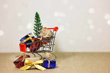 Merry Christmas, Happy New Year and Boxing day concept. Present boxes, shopping cart, pine tree and house models on light brown background.