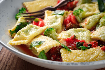 Italian square ravioli with basil, tomato sauce and broccoli in a plate close-up on wood. Pasta ravioli with vegetables