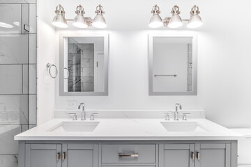 An elegant, remodeled bathroom with a grey vanity and bronze hardware. The shower has a large...