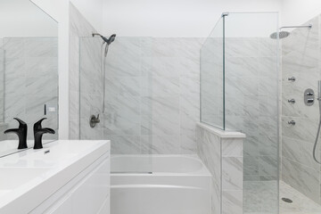 An all white master bathroom with black hardware and faucets showing the vanity and shower with the...
