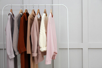 Rack with different stylish clothes near grey wall. Space for text