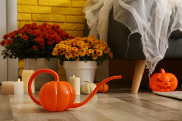 Pumpkin shaped watering can on floor in room, space for text. Halloween decor