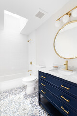 A white bathroom with a blue vanity cabinet, granite countertop, pattern tile flooring, and gold...