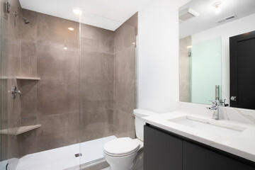 A luxurious bathroom with a grey vanity cabinet, a white marble countertop, and brown tiles on the shower walls.