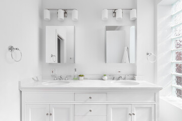 Fototapeta na wymiar A bright, white bathroom with a marble countertop, chrome hardware and faucets, and block window.