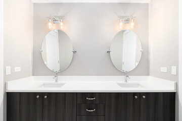 A luxury bathroom with a wooden vanity cabinet, large marble countertop, and lights mounted above...