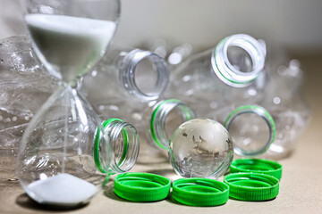 Plastic pollution. Empty plastic bottle, plastic bag and wolrd globe crystal glass with sand running through hourglass on table. Countdown timer for global warimg concept.