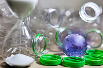 Plastic pollution. Empty plastic bottle, plastic bag and wolrd globe crystal glass with sand running through hourglass on table. Countdown timer for global warimg concept.
