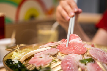 Action of people hand using chopstick to grilling a piece of slice pork meat in BBQ meal. Eating food close-up action photo. Selective focus.