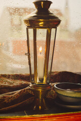 Old candle lamp on window with rain drops, old book, warm coat and cup of hot chocolate on a rainy...