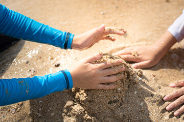 Close-up action at kid hand is playing sand on beach ground.  Recreation and holiday activity scene. Selective focus.