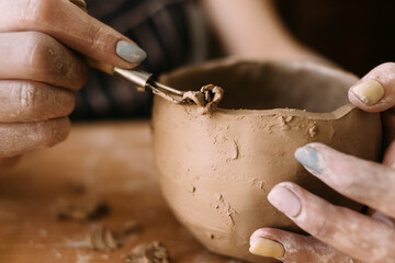 the hands of a clay potter carve a pattern on the bowl. Side view. Ceramics and clay for creativity...