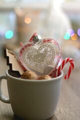 Mug filled with various Christmas ornaments, lit candles and colorful bokeh lights in the background. Selective focus.