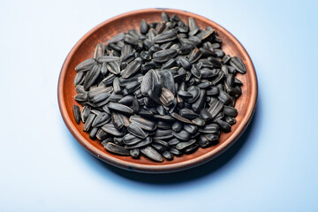 Black sunflower seeds on a plate on a blue background.