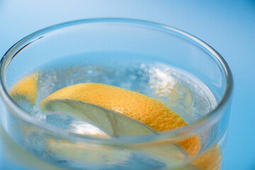 Lemon slice in a glass of fresh water on a blue background close-up close-up.