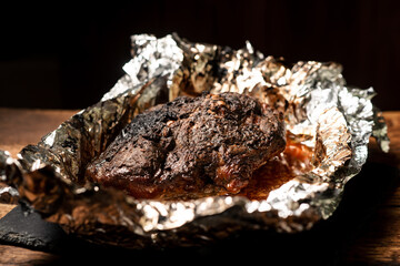 A large piece of baked meat with spices wrapped in foil in the oven.