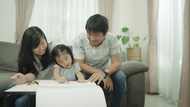 Asian Family parents play with daughters at the home table. adult parent father teaching cute small children girls learning creative activity enjoying happy high five with daddy and mom on holiday.