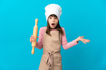 Little girl holding a rolling pin isolated on blue background with shocked facial expression