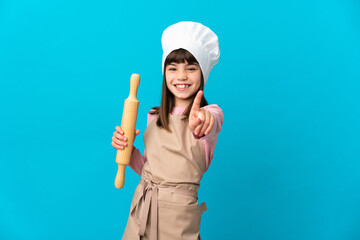 Little girl holding a rolling pin isolated on blue background showing and lifting a finger