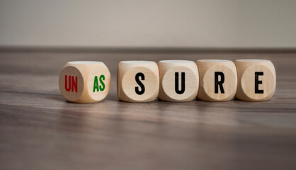 Cubes, dice or blocks with unsure and assure on wooden background