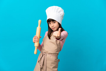Little girl holding a rolling pin isolated on blue background making money gesture