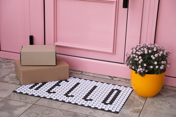 Cardboard boxes on stylish door mat and beautiful flowers near entrance