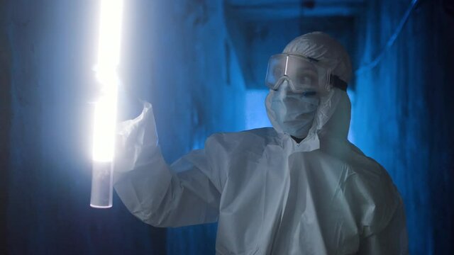 Hazmat suit wearing woman explores a dark tunnel. Female in protective suit, mask and glasses with flashlight walking in dark tunnel, looks around