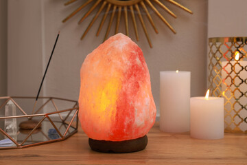 Himalayan salt lamp, candles and crystals on wooden table near white wall indoors - obrazy, fototapety, plakaty