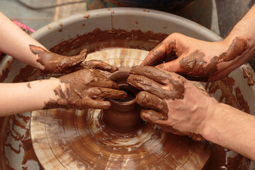 The child moulds from clay a pot on a potter's wheel. Adults help the child to work with clay.