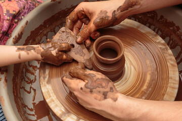 The child moulds from clay a pot on a potter's wheel. Adults help the child to work with clay.