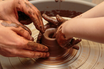 The child moulds from clay a pot on a potter's wheel. Adults help the child to work with clay.