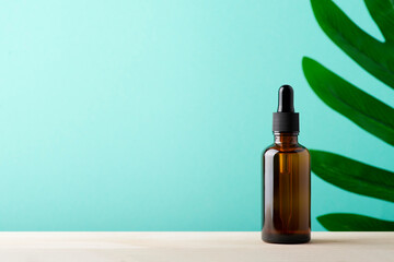 Amber glass dropper bottle with black lid. Skincare concept with mint green and wooden surface...