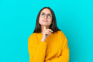 Young Ukrainian woman isolated on blue background With glasses and looking up