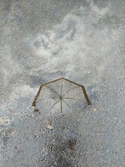 Weightless reflection of an umbrella and clouds in a puddle on the asphalt road