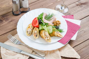 Crepes stuffed with ham decorated with herbs on a white plate