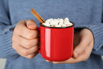 Woman holding cup of delicious hot chocolate with marshmallows and cinnamon stick, closeup