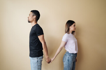 Multiethnic couple holding hands. Young Caucasian woman and African male arms together on beige background. Family concept