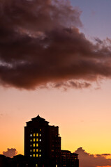 Naklejka premium front view, far distance of a concrete building with lite window at dusk with threatening thunder clouds